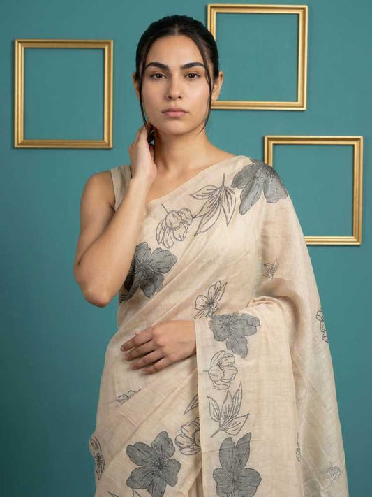 Woman wearing a beige saree with floral patterns against a teal background with gold frames.
